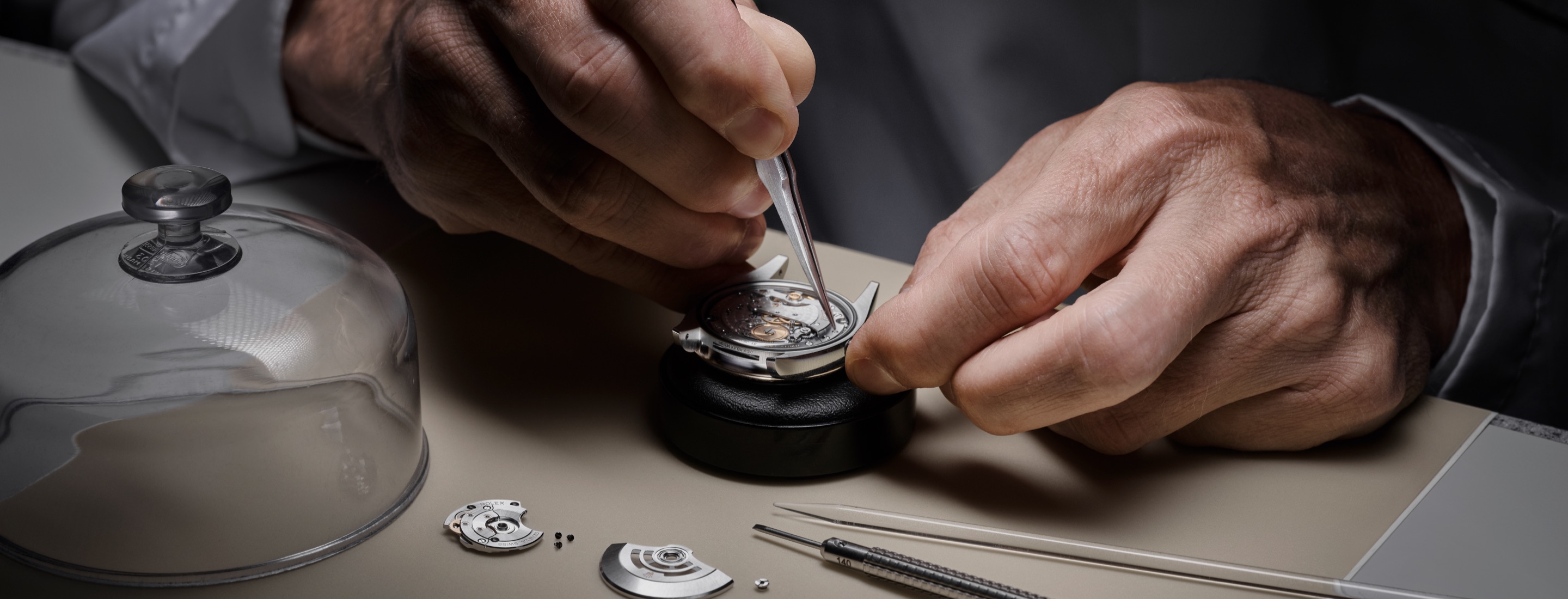Rolex Uhrmacher bei der Montage eines Manufakturwerks unter Glasglocke